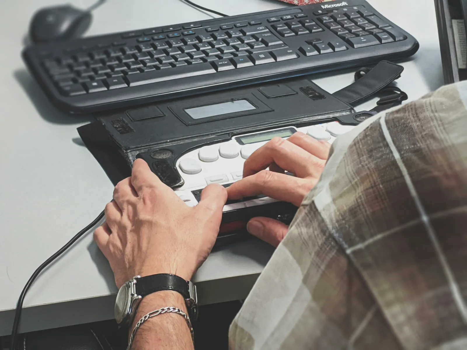Hands on a refreshable braille display in front of a keyboard